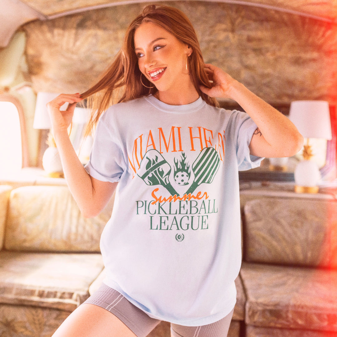 White unisex tee with Miami HEAT Pickleball League graphic in orange and green, worn by smiling woman. - Court Culture HEAT Pickleball League Unisex Tee