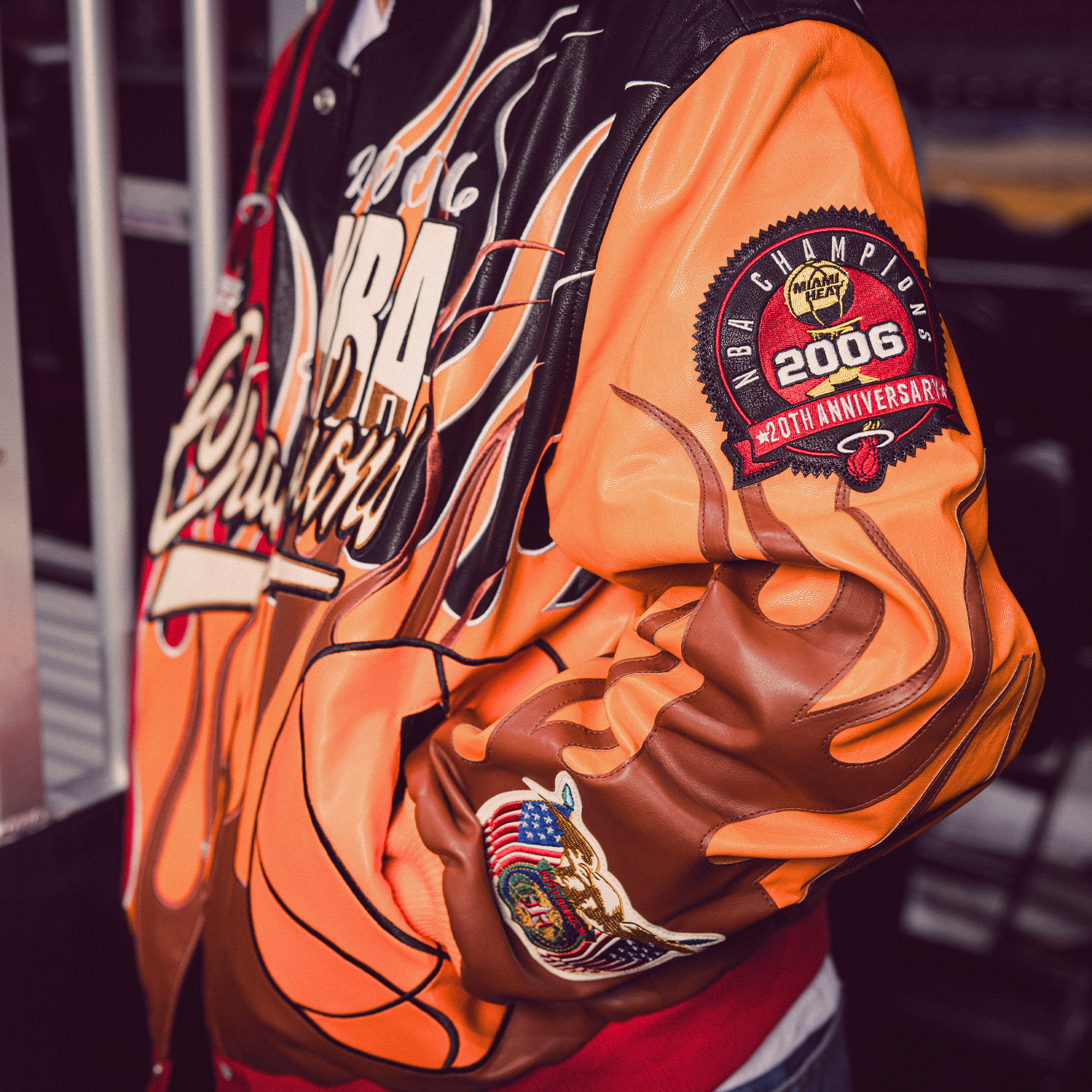 A person wearing the Court Culture Miami HEAT x Jeff Hamilton 2006 Championship Legacy Jacket, featuring vibrant NBA Finals graphics, a flaming basketball, and a patch honoring the team's 2006 NBA title.