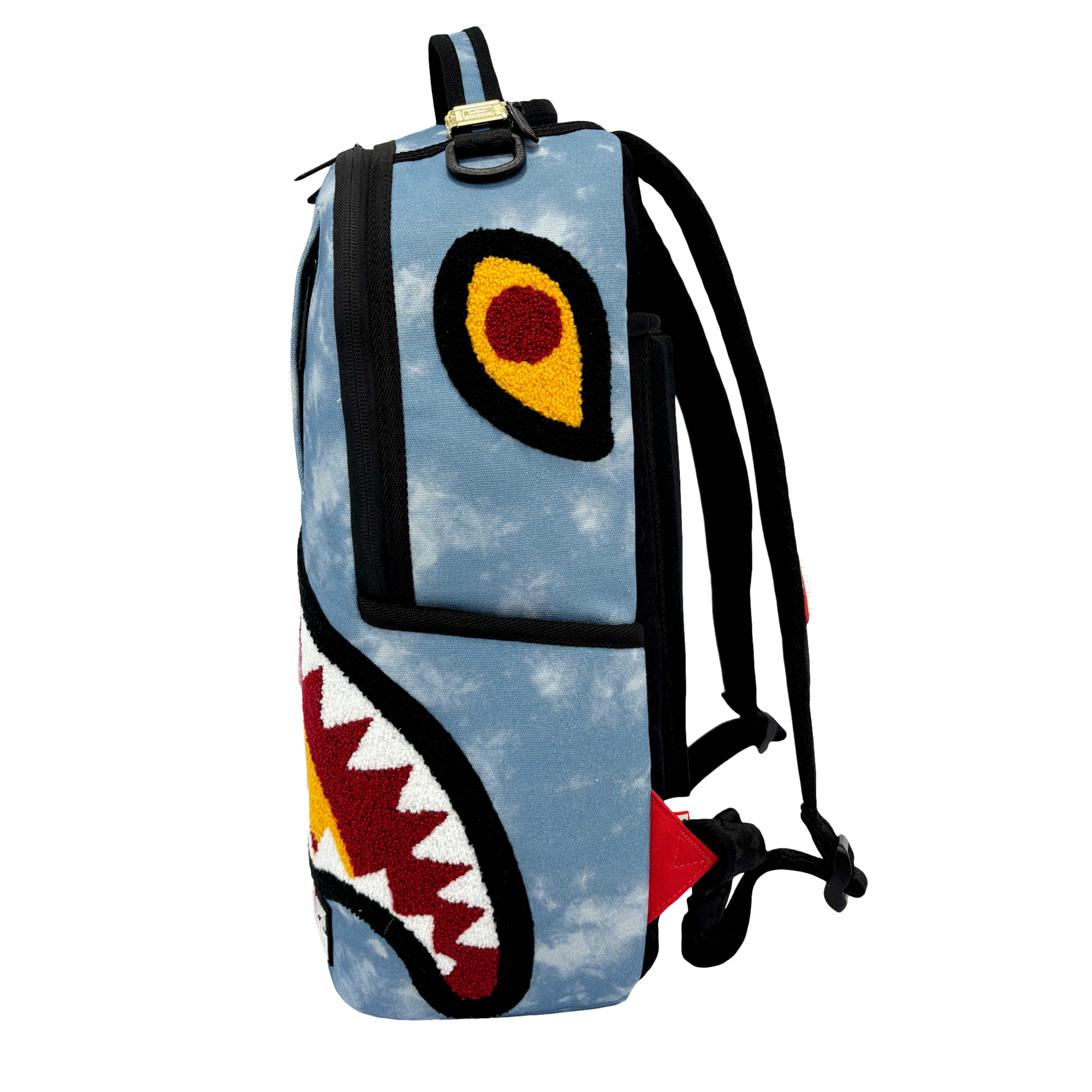 The Court Culture x Sprayground Miami HEAT Tie-Dye Jaw Backpack by Sprayground is a limited edition blue denim backpack distinguished by its striking shark face design—complete with fierce teeth, yellow and red eyes, black straps, an embroidered logo, and a red tag on the side—all set against a plain white background.