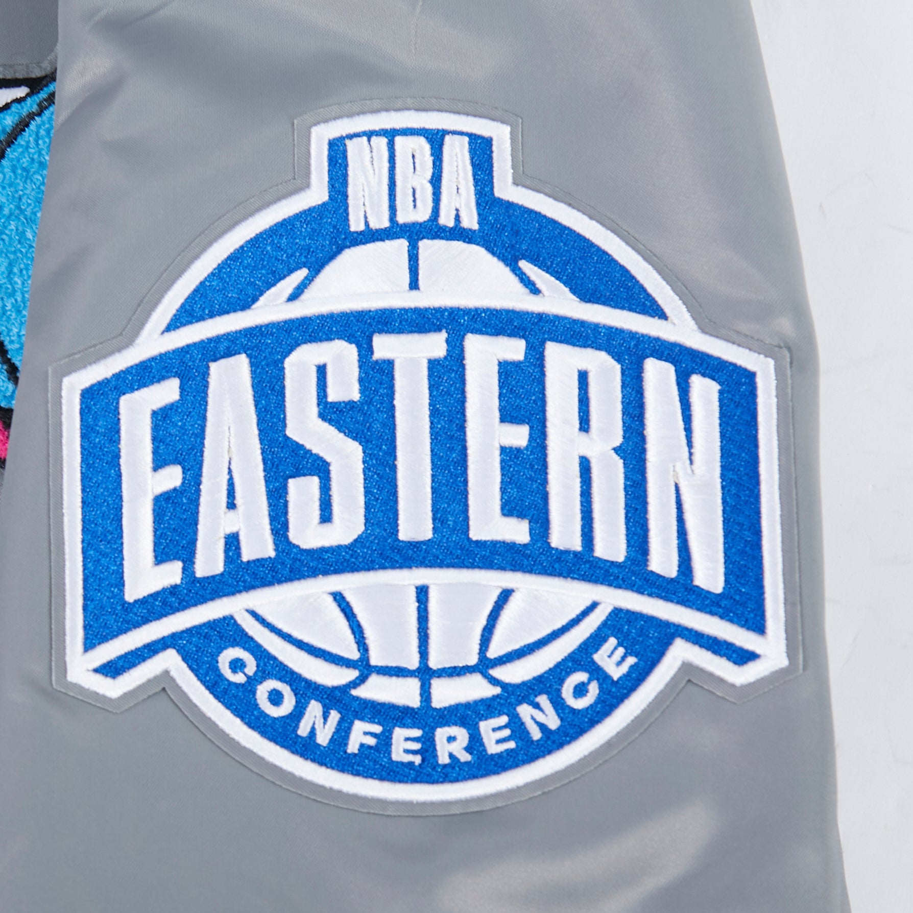 The Pro Standard Miami HEAT Original Vice Nights Satin Jacket features a blue and white NBA Eastern Conference logo patch on gray polyester, highlighted with a basketball graphic and bold lettering. Machine washable for easy care.