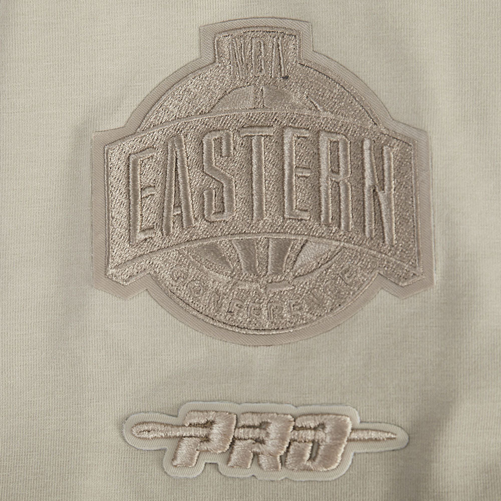 A close-up of the Pro Standard Miami HEAT Original Vice Nights Beige Women's Boxy Tee shows beige cotton spandex fabric with two embroidered patches: a large EASTERN patch and a smaller stylized PRO patch. Wash with like colors.