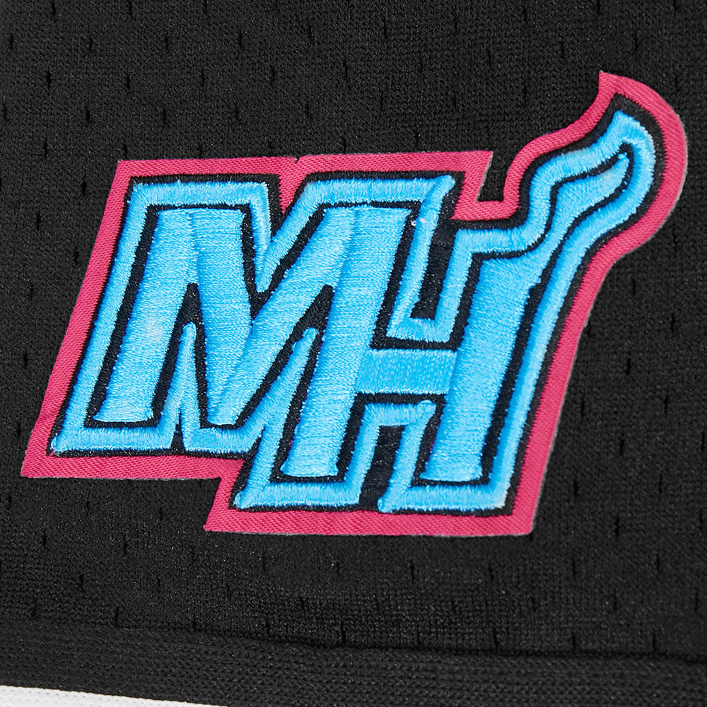 A close-up of the Pro Standard Miami HEAT Original Vice Nights Youth Mesh Shirt shows black polyester fabric with an embroidered MH logo in bold blue and pink, flame-detailed, by Pro Standard. It features a standard fit and is machine washable.