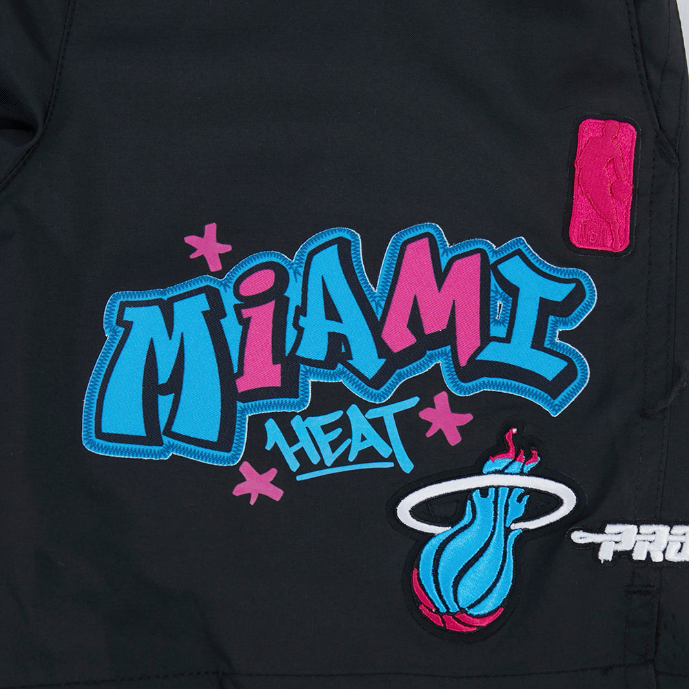 The image shows Pro Standard Miami HEAT Original Vice Nights Youth Shorts in black, with a graffiti-style blue and pink Heat logo, flaming basketball emblem, small pink patch, relaxed fit polyester fabric, and easy machine wash care.