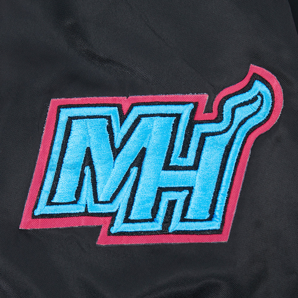 The Pro Standard Miami HEAT Original Vice Nights Youth Satin Jacket features a bold embroidered MH logo in blue with pink and black outline, including a wavy flame-shaped H, on black polyester. Standard fit and machine washable for easy care.