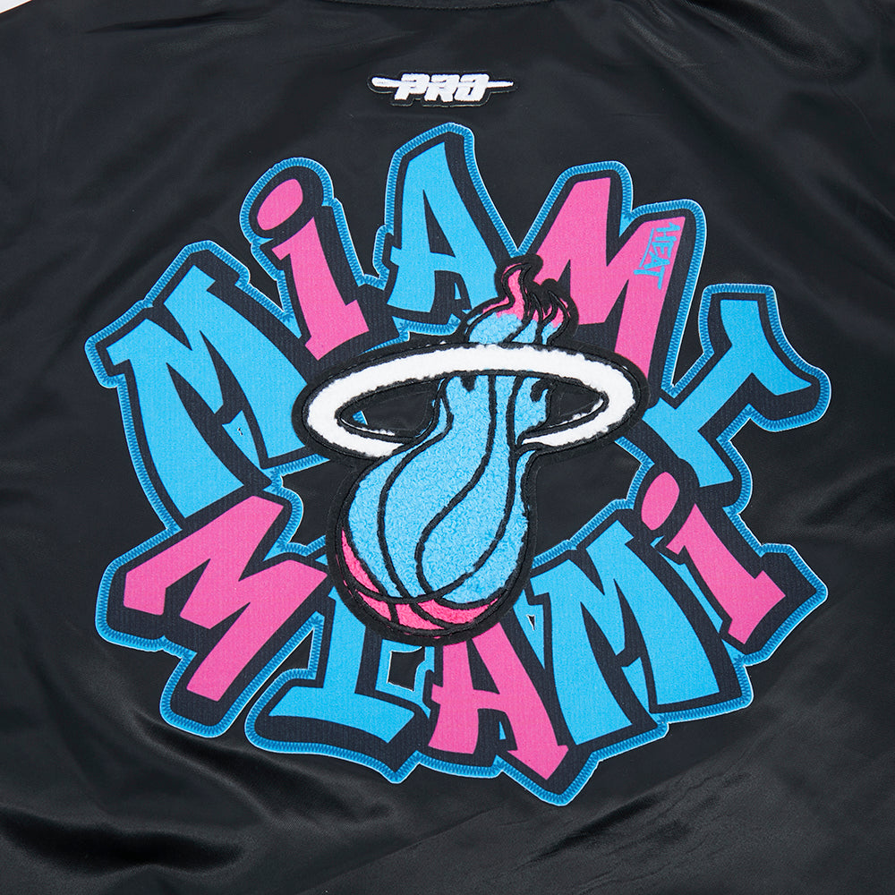 The Pro Standard Miami HEAT Original Vice Nights Youth Satin Jacket features a black polyester fabric with a blue and pink Miami graphic, flaming basketball logo, 