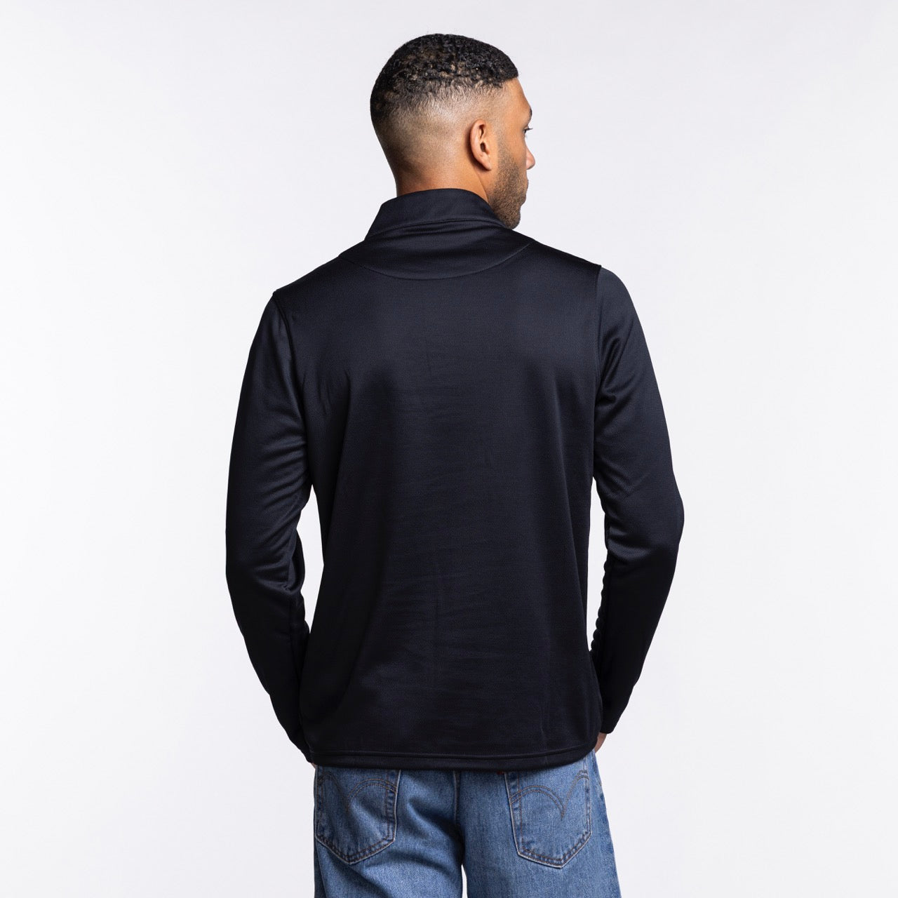 A man wearing a Nike Miami HEAT Original Vice Nights 1/4 Zip Jacket in black polyester and blue jeans, standard fit, stands facing away from the camera against a plain white background.