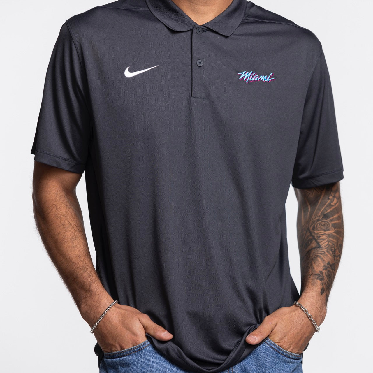 A person wears a dark gray Nike Miami HEAT Original Vice Nights Polo with colorful 