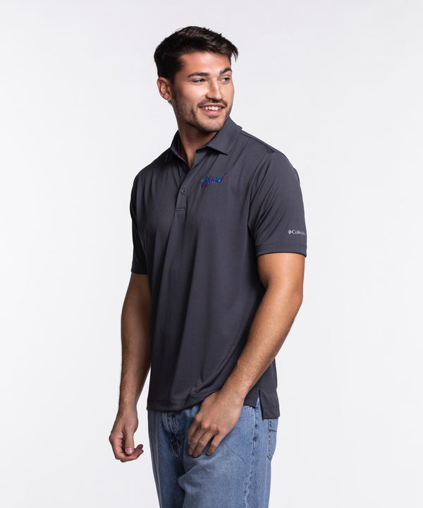 A man with short brown hair and a trimmed beard wears a Columbia Miami HEAT Original Vice Nights Drive Polo by Columbia Outdoor and blue jeans, standing against a plain white background.