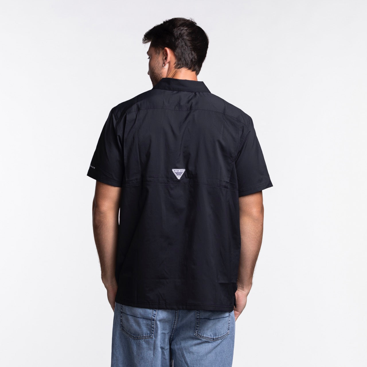 A man faces away from the camera, wearing a Columbia Outdoor Miami HEAT Original Vice Nights Slack Tide Shirt and light blue jeans against a plain white background.