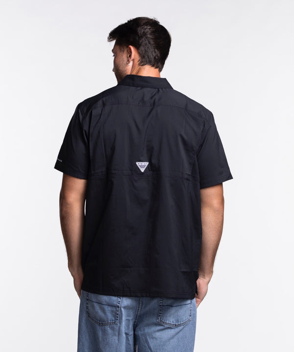 A man with short dark hair and a beard wears the Columbia Miami HEAT Original Vice Nights Slack Tide Shirt by Columbia Outdoor and light blue jeans, standing against a plain white background.