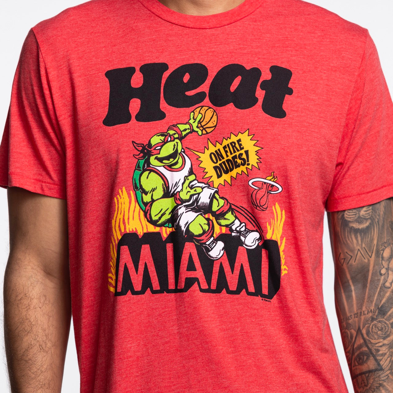 Wearing the Homage Miami HEAT Red TMNT Tee by Homage, featuring a standard fit and a polyester-cotton-rayon blend, cartoon turtle playing basketball, Miami Heat graphics, “Heat Miami,” “On fire dudes!” text with flames. Machine wash cold.