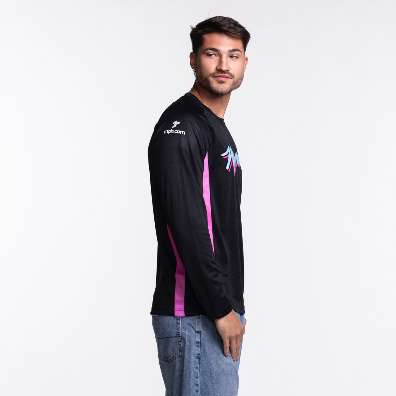 A man with short dark hair and a beard models the Nike Miami HEAT Original Vice Nights Shooting Shirt by Nike—standard fit, long-sleeve, black with pink stripes and blue-purple graphics—paired with light blue jeans. Wash with like colors.