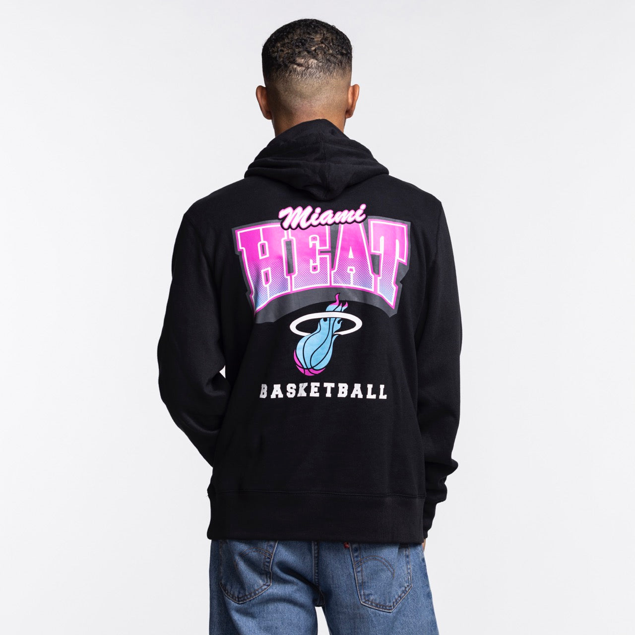 A person faces away, wearing the '47 Brand Miami HEAT Original Vice Nights Hoodie in black cotton-polyester, featuring Miami Heat Basketball and logo in pink, white, and blue on the back. Machine washable. Plain white background.