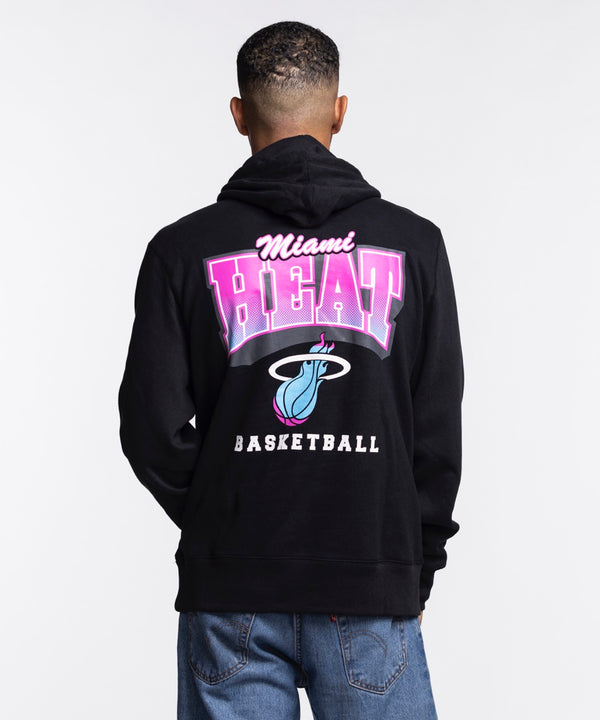 A man faces forward in a '47 Brand Miami HEAT Original Vice Nights Hoodie, featuring the basketball logo. The black cotton-polyester hoodie is machine washable and paired with light blue jeans against a plain white background.