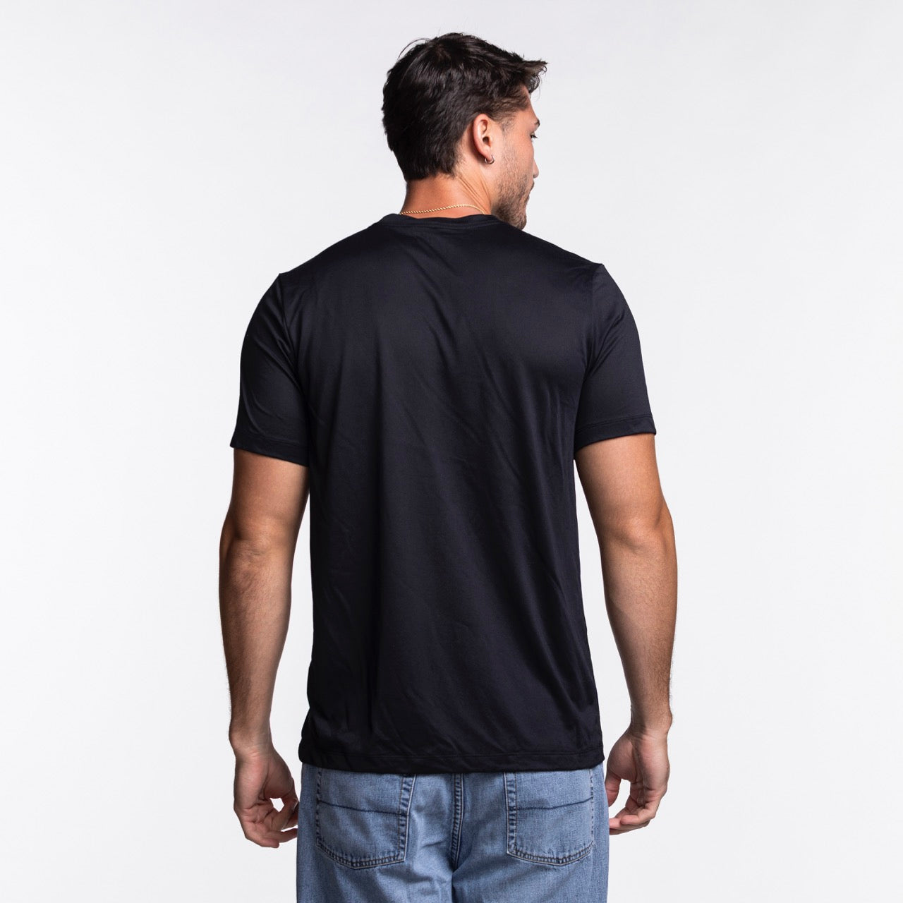 A man with short dark hair is standing with his back to the camera against a plain white background, wearing a black Nike Miami HEAT Original Vice Nights Legend Tee and blue jeans.