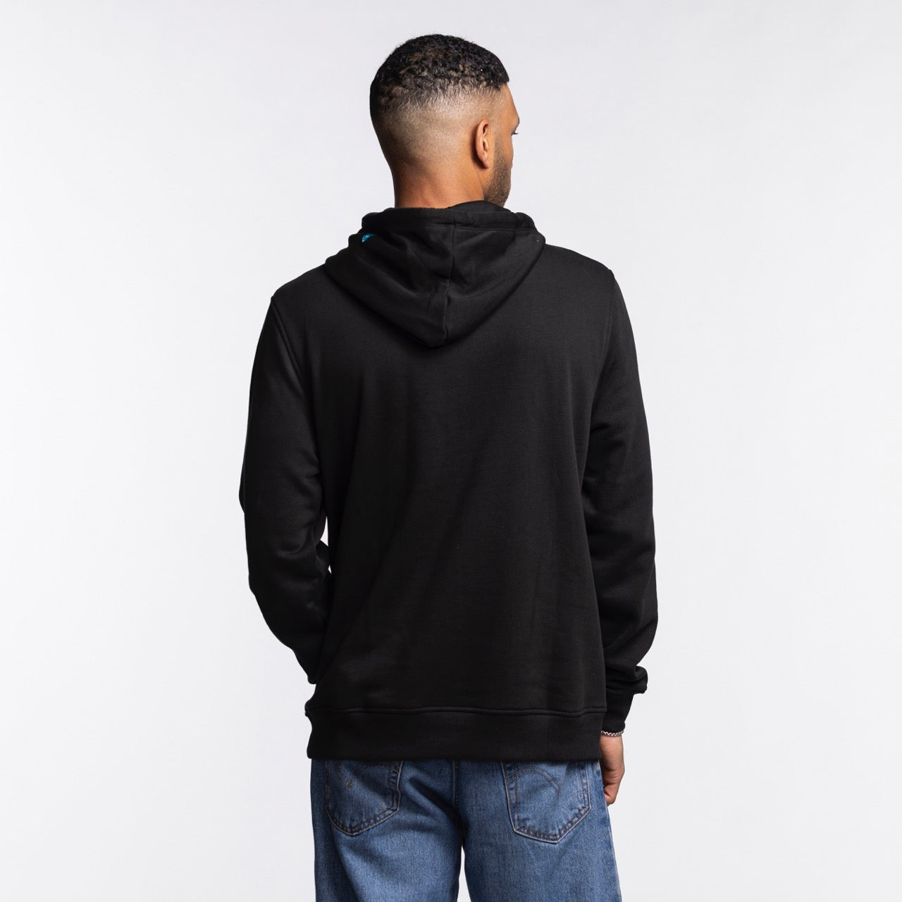 A man stands with his back to the camera, wearing a New Era Miami HEAT Original Vice Nights Miami HEAT Logo Hoodie in black and blue jeans, set against a plain white background.