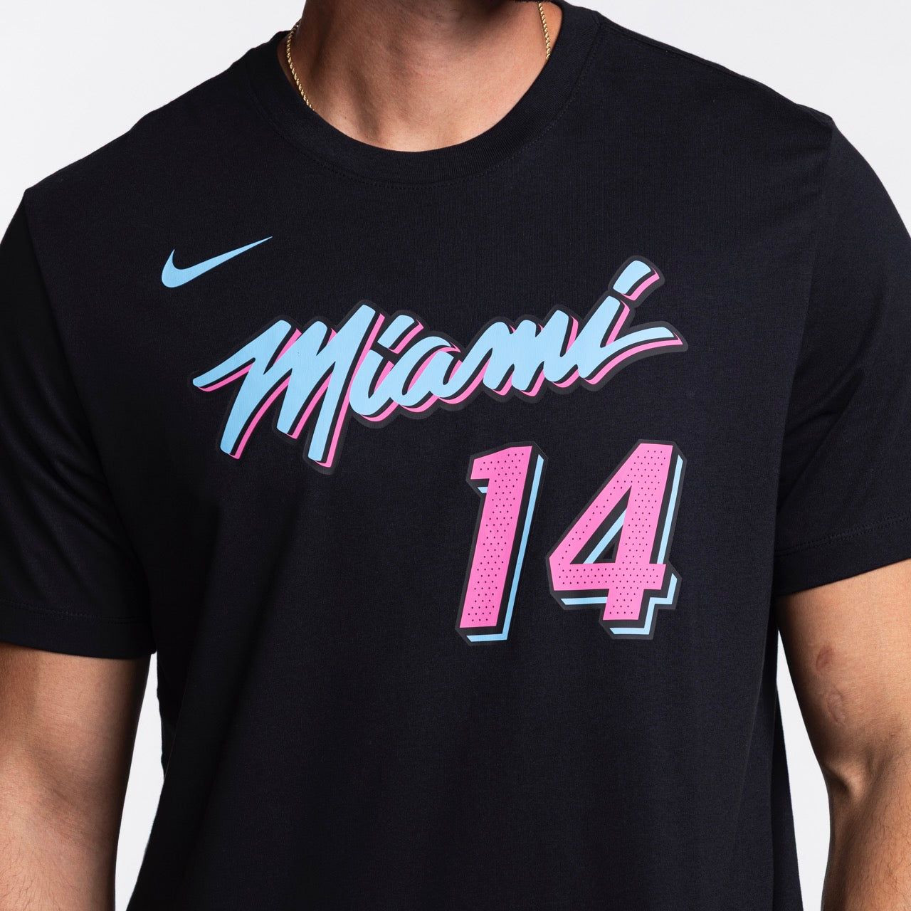 Someone wearing the Nike Tyler Herro Original Vice Nights Name & Number Tee—a black, standard fit cotton shirt with “Miami” in blue and pink script, Herro’s number 14 below, a blue Nike logo on the left shoulder; machine washable.