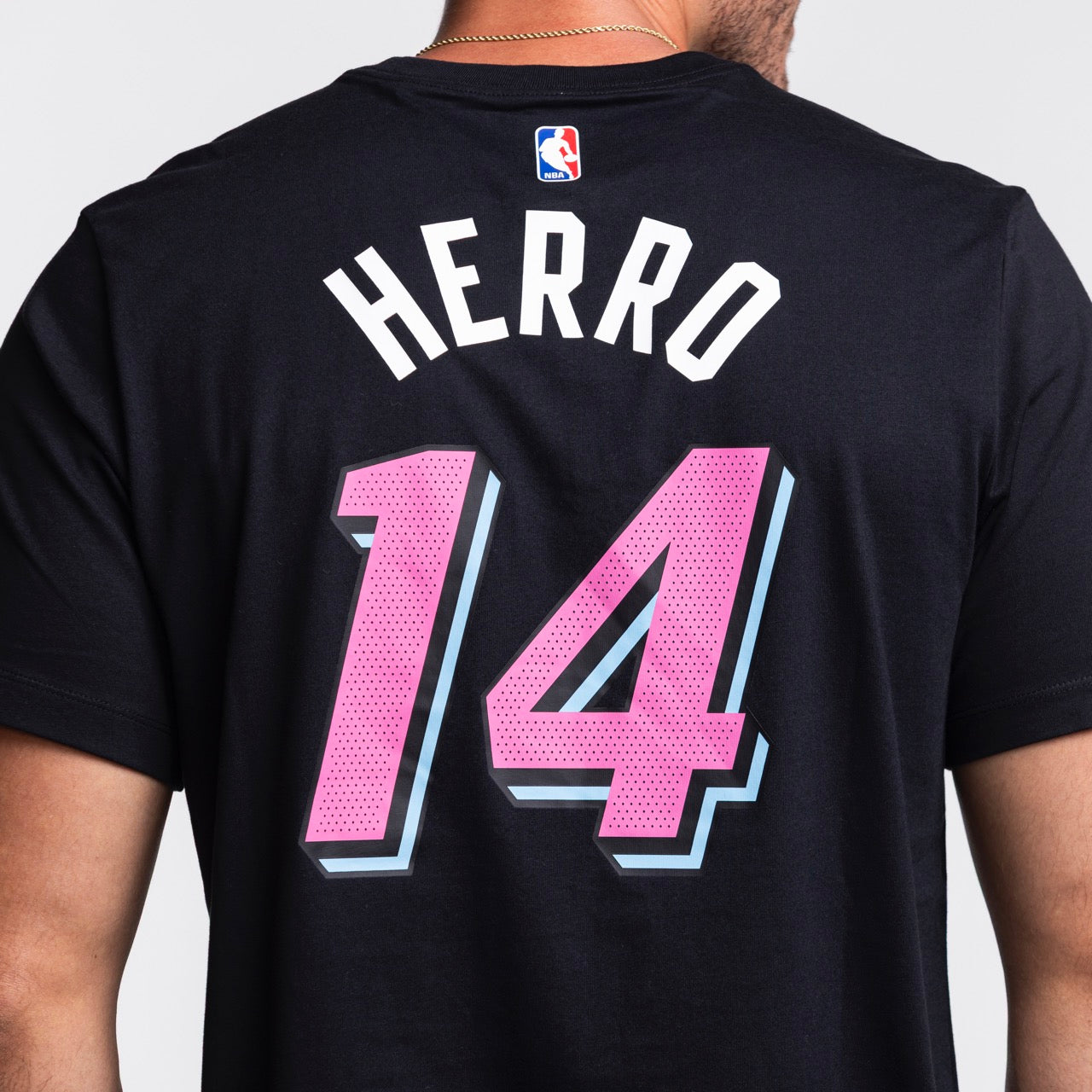 A person wearing the Nike Tyler Herro Original Vice Nights Name & Number Tee, a black cotton shirt featuring HERRO and number 14 in pink and blue, styled like an NBA jersey and easy to wash.