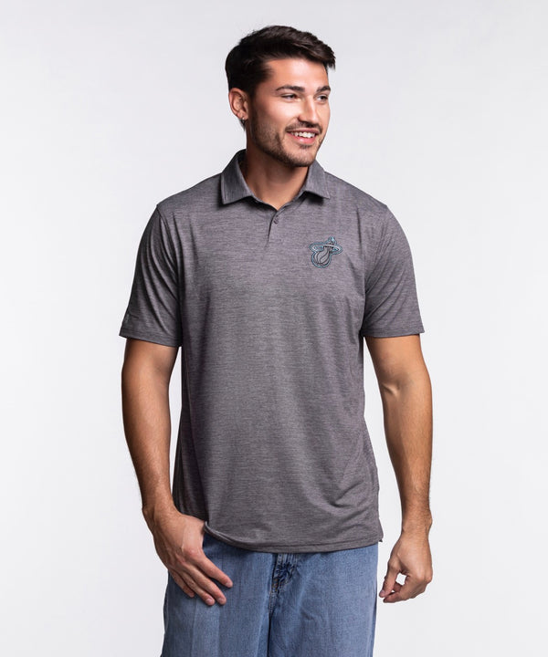 A man with short dark hair and a beard wears the Antigua Miami HEAT Original Vice Nights Polo by Antigua— a standard fit gray short-sleeve polo with a small chest logo—paired with blue jeans, standing and smiling against a plain light background.