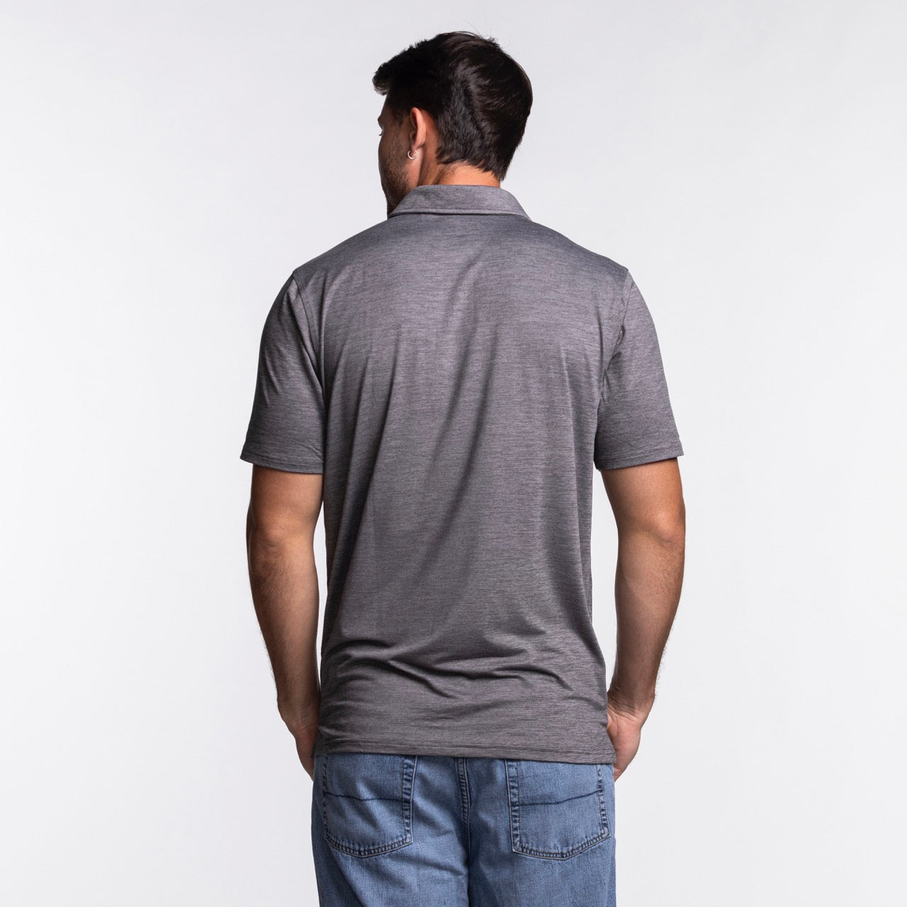 A man faces away from the camera, dressed in an Antigua Miami HEAT Original Vice Nights Polo by Antigua and blue jeans, set against a plain white background.