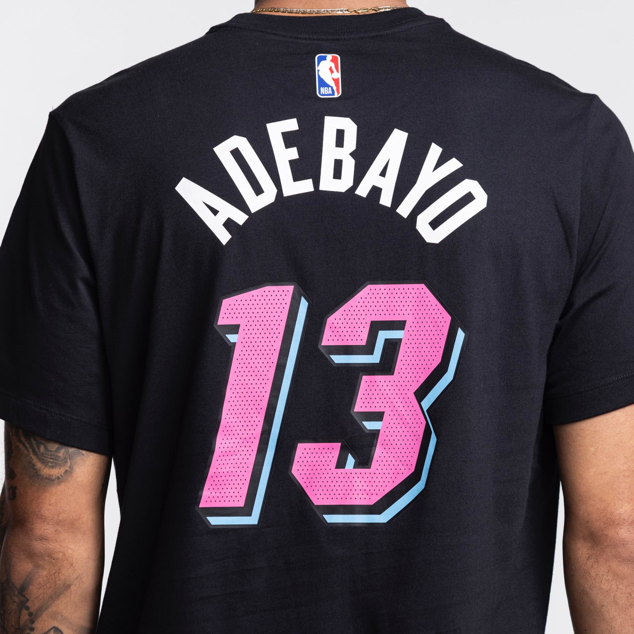 A person wearing a black Nike Bam Adebayo Original Vice Nights Name & Number Tee featuring 