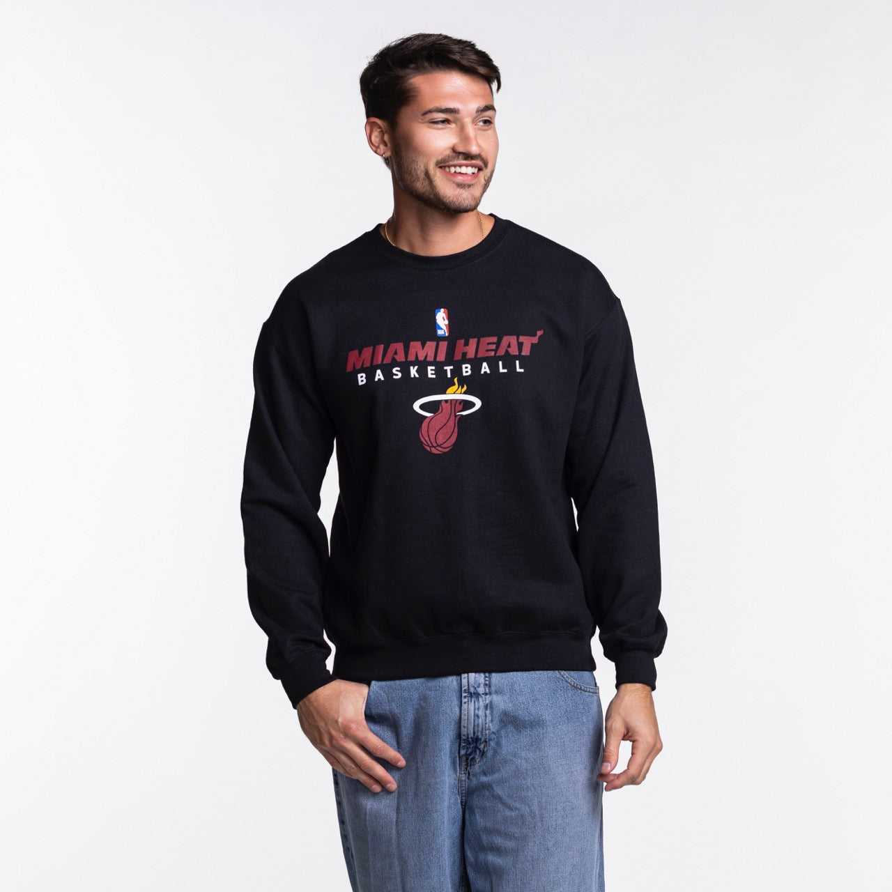 A man smiles in an Item Of The Game Miami HEAT NBA Basketball Crewneck, crafted from soft cotton-polyester, paired with blue jeans against a plain white background.