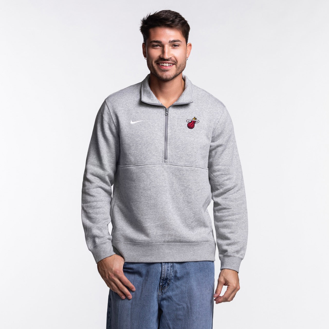 A man smiles in a Nike Miami HEAT Fleece 1/2 Zip Jacket and blue jeans, standing against a plain white background.