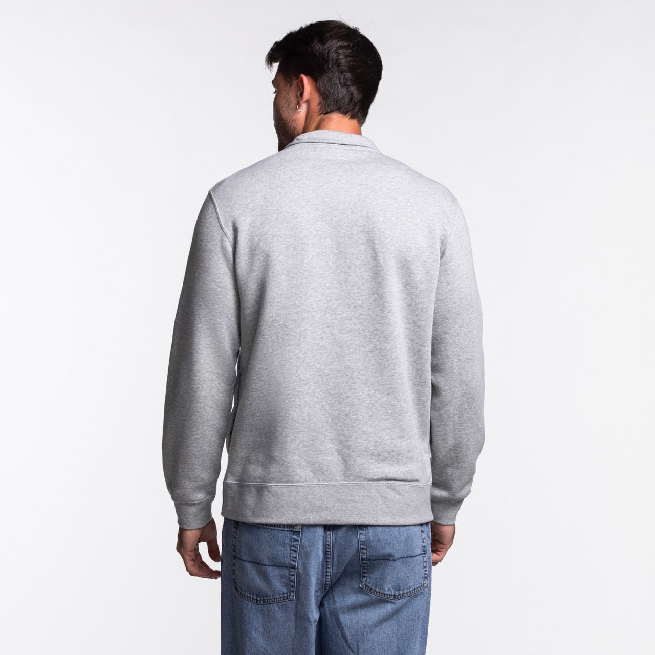 A man wearing a Nike Miami HEAT Fleece 1/2 Zip Jacket and blue jeans stands facing away from the camera against a plain white background.