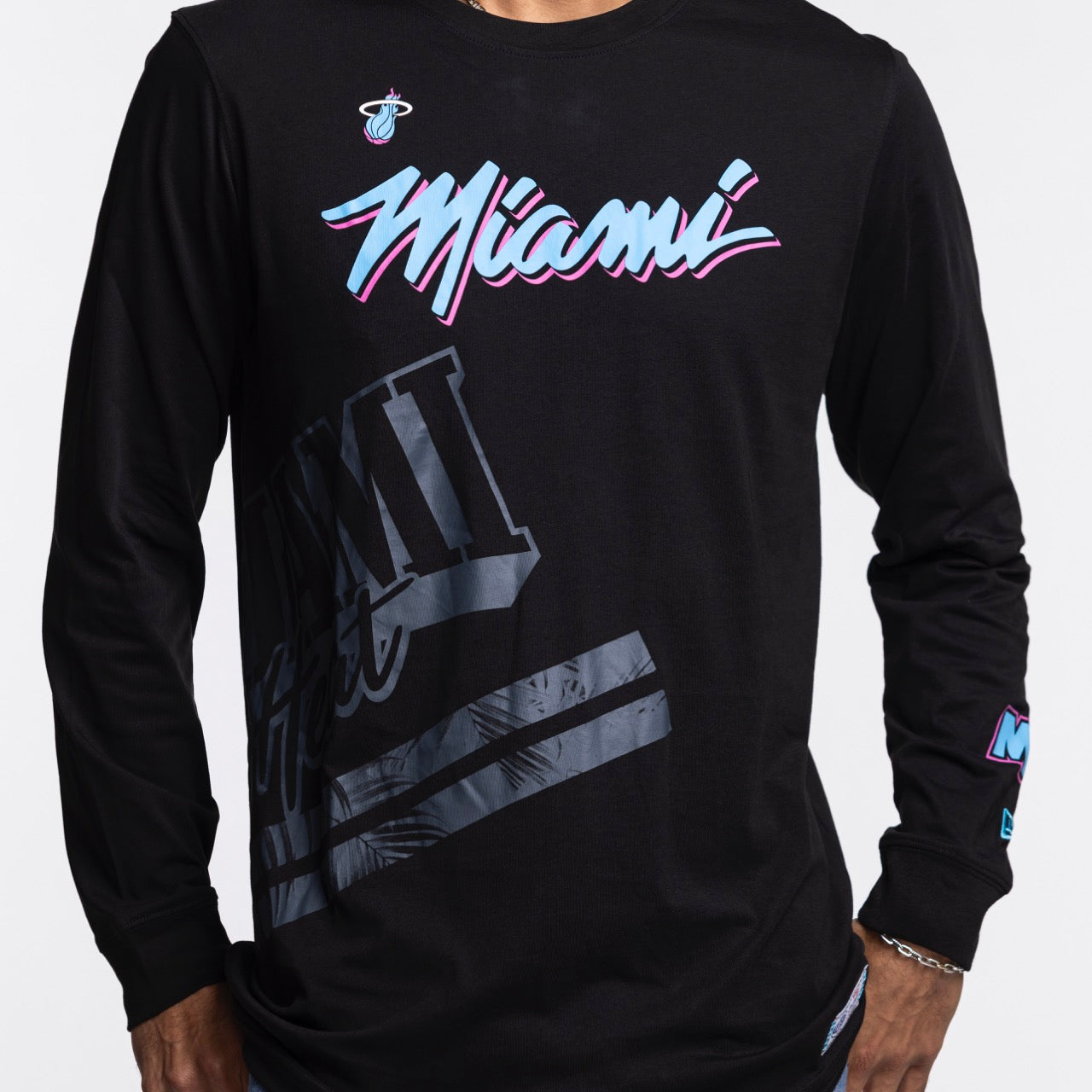 A person wears the New Era Miami HEAT Original Vice Nights Wordmark Long Sleeve Tee—a black, standard fit 100% cotton shirt featuring 