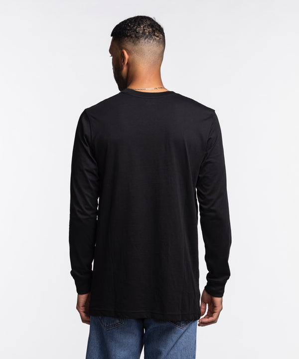 A man stands facing forward against a plain white background wearing a New Era Miami HEAT Original Vice Nights Wordmark Long Sleeve Tee, a black 100% cotton shirt featuring colorful Miami text and graphic designs on the front and sleeve.