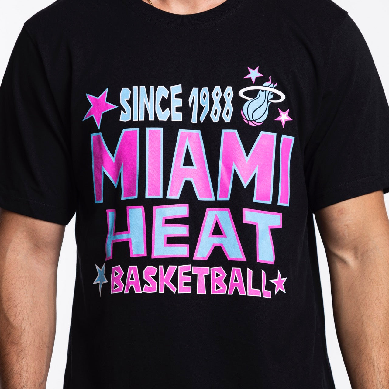A person wears the Sportiqe Miami HEAT Original Vice Nights Star Tee—a black, standard fit 100% cotton shirt with colorful 