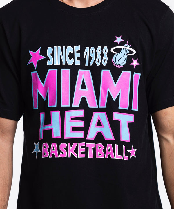A man faces forward in the Sportiqe Miami HEAT Original Vice Nights Star Tee—a black, 100% cotton, standard-fit t-shirt with colorful text and stars—paired with light blue jeans against a plain white background.