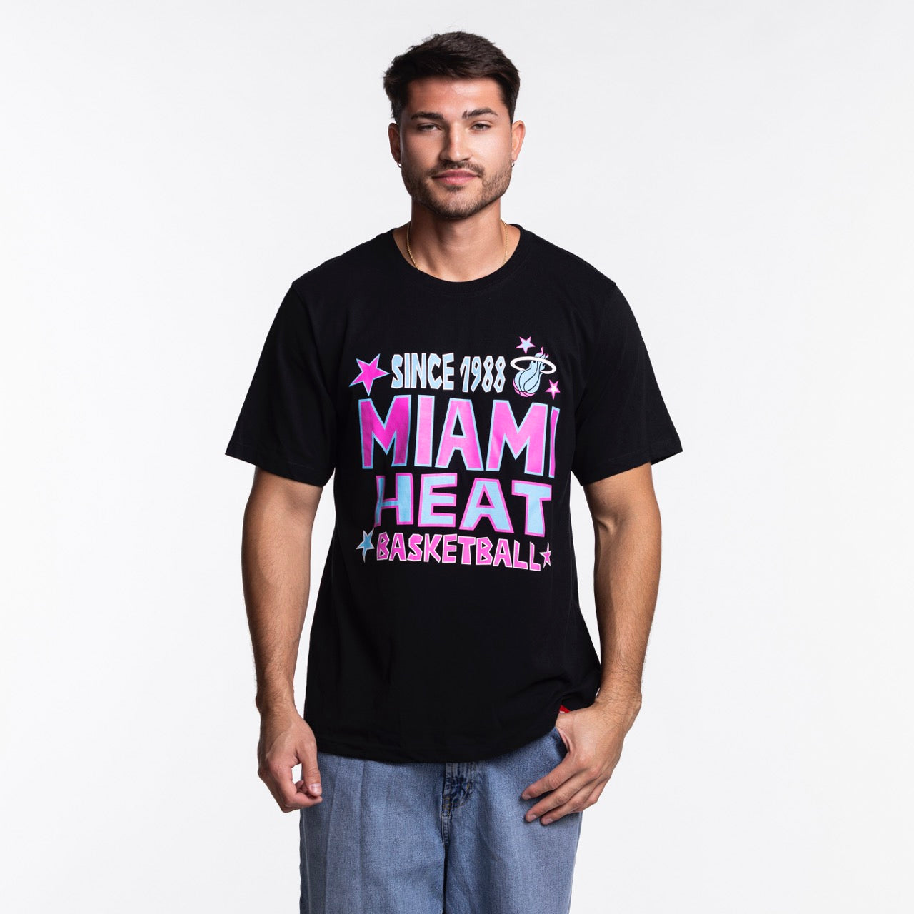 A man faces forward in the Sportiqe Miami HEAT Original Vice Nights Star Tee—a black, 100% cotton, standard-fit t-shirt with colorful text and stars—paired with light blue jeans against a plain white background.