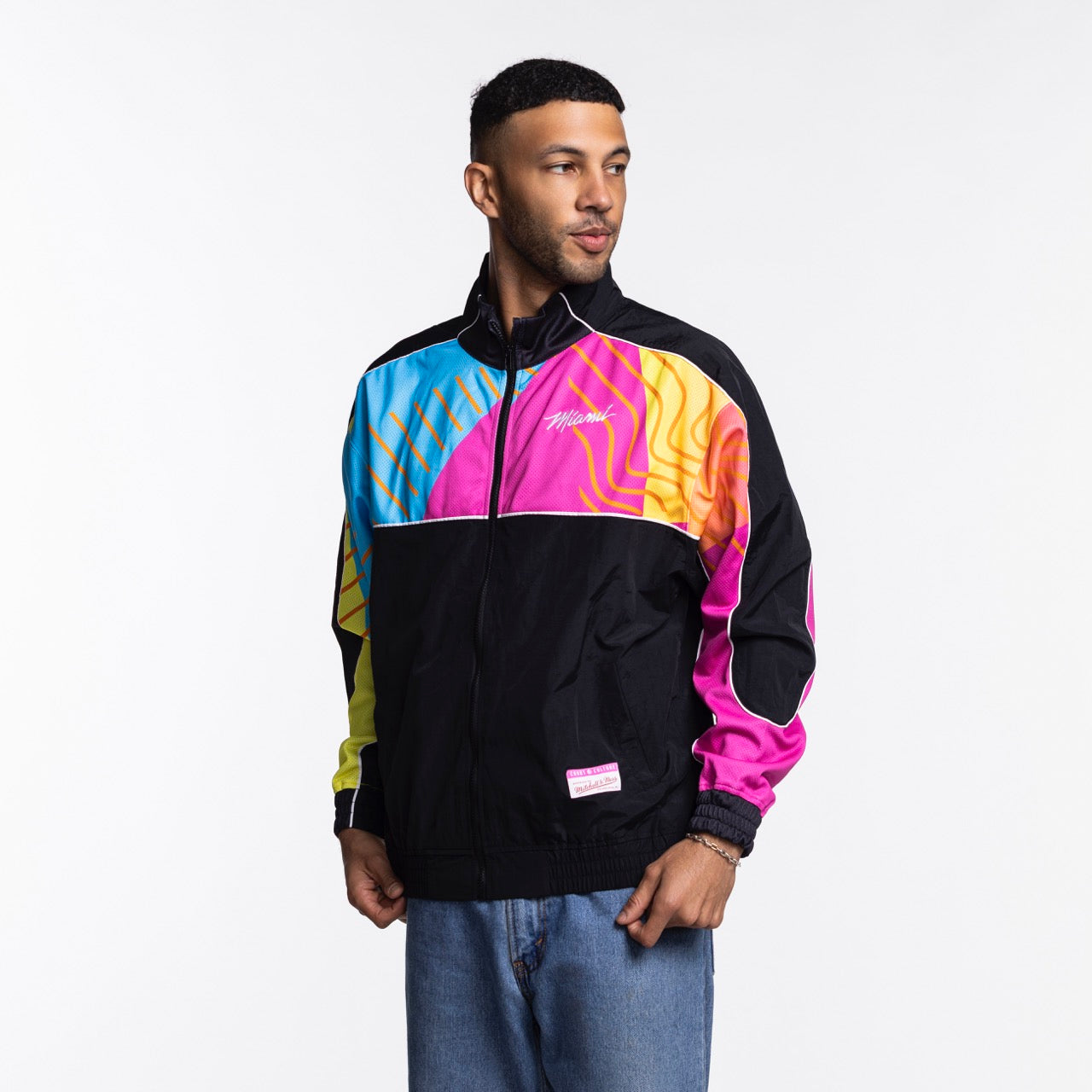 A man stands against a white background, looking left with his hands at his sides, wearing the Court Culture x Mitchell & Ness Original Vice Nights 