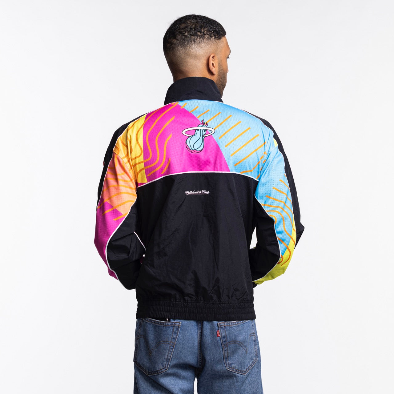 A man with short dark hair and blue jeans faces away, wearing the Court Culture x Mitchell & Ness Original Vice Nights 