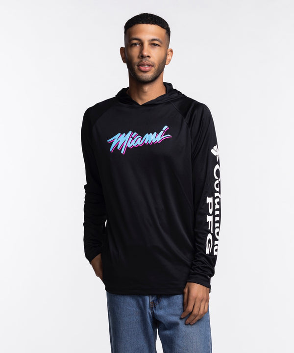 A man stands against a white background wearing the Columbia Miami HEAT Original Vice Nights Long Sleeve Hoodie Tee by Columbia Outdoor in black, featuring colorful 