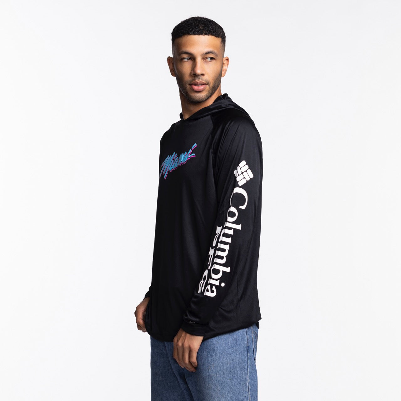A man wears a Columbia Outdoor Miami HEAT Original Vice Nights Long Sleeve Hoodie Tee in black, featuring colorful 