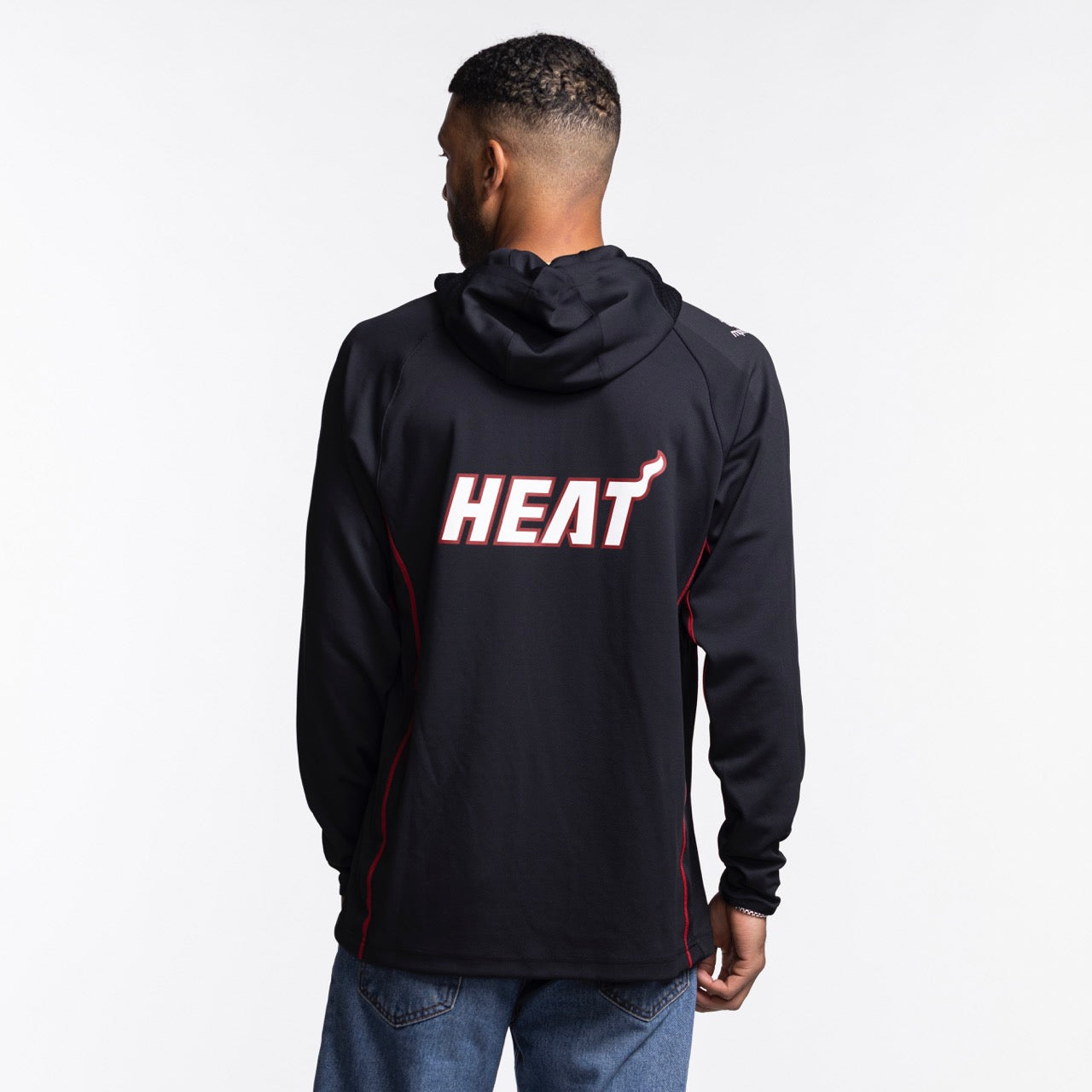 A man faces away from the camera wearing a Nike Miami HEAT On-Court 1/4 Zip Hoodie in black with bold white and red 