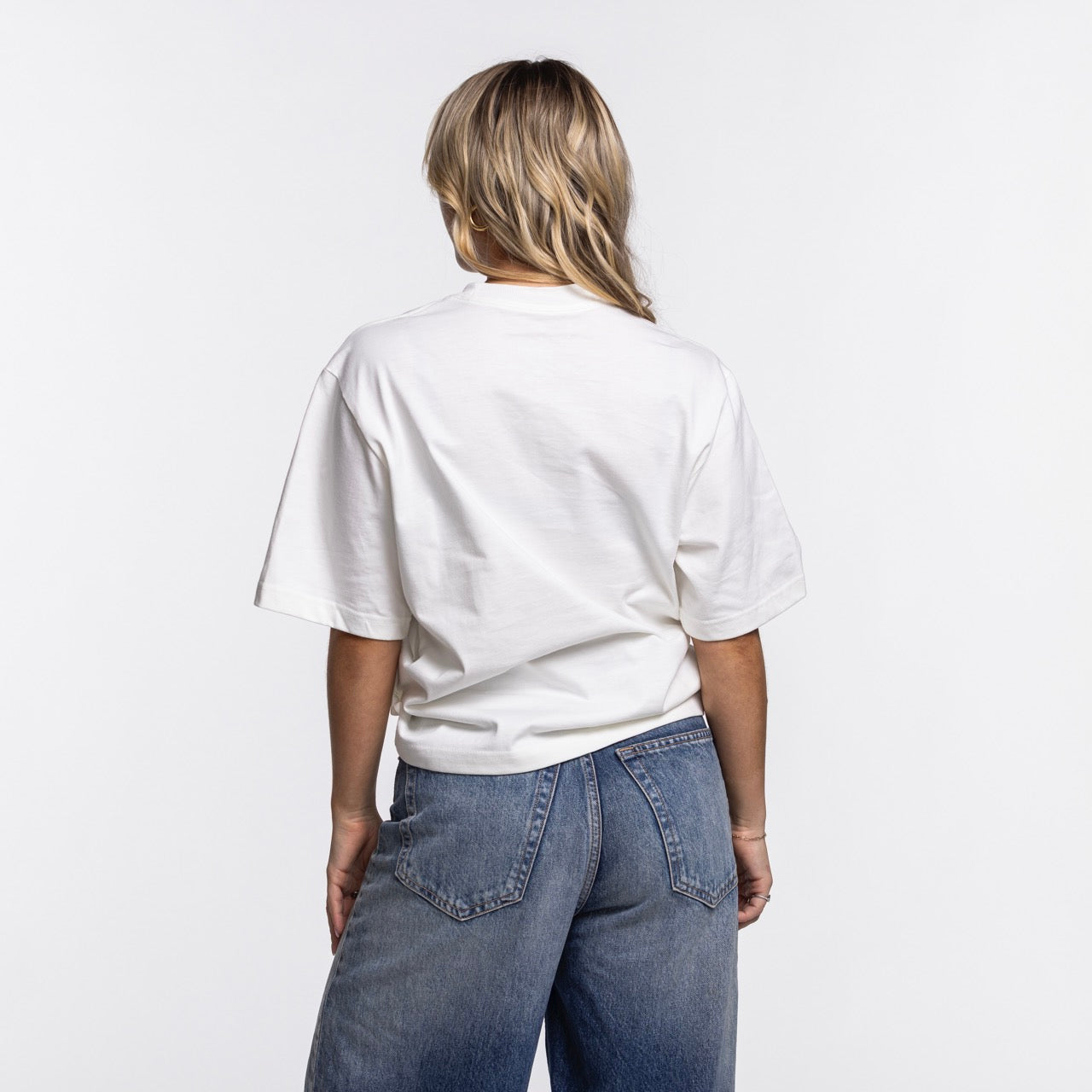 A woman with long blonde hair stands with her back to the camera, wearing the Nike Miami HEAT Original Vice Nights Women's Tee by Nike and blue jeans against a white background. For best results, wash with like colors.