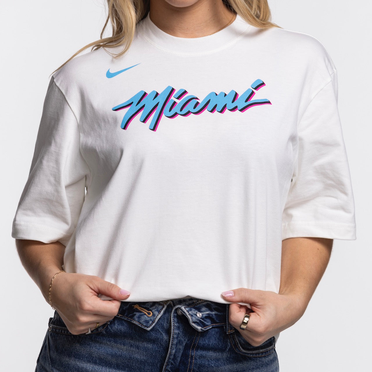 A person wears the Nike Miami HEAT Original Vice Nights Women's Tee—a loose-fit white cotton shirt with colorful 