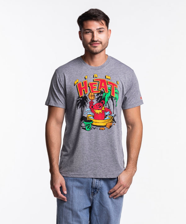 A man stands facing forward in blue jeans, wearing the Homage Miami HEAT Grateful Dead Bear Tee by Homage—a comfortable standard fit T-shirt made from polyester, cotton, and rayon that’s easy to machine wash cold.