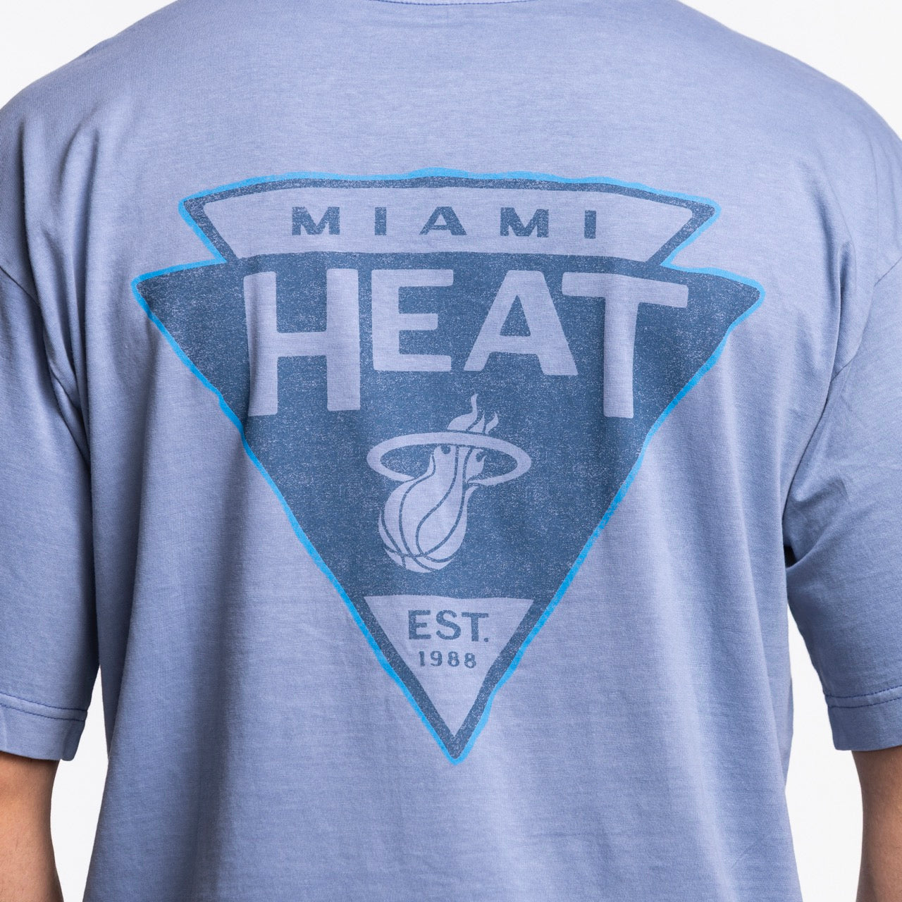 A person wears the '47 Brand Miami HEAT Original Vice Nights Switchback Tee, featuring a large team logo and “EST. 1988” on the back, crafted from 100% cotton and machine washable for easy care.
