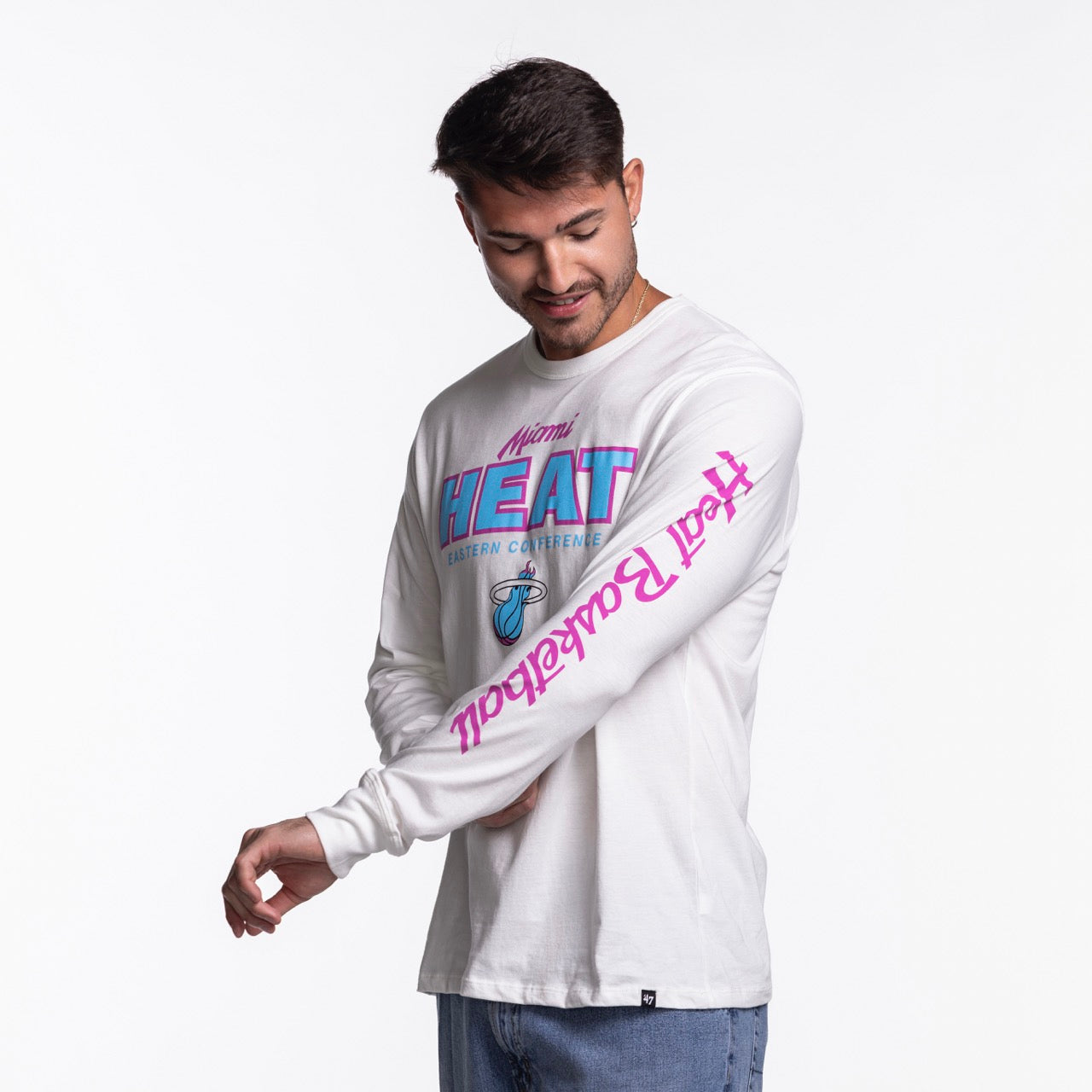 A man smiles and looks down, holding his sleeve, while wearing the '47 Brand Miami HEAT Original Vice Nights White Long Sleeve Tee against a plain white background.