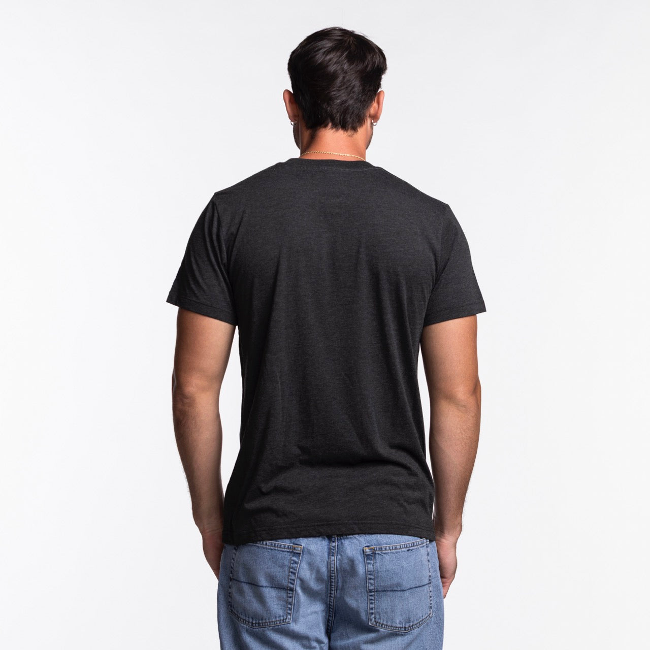 A man with short dark hair, wearing the Homage Miami HEAT Original Vice Nights City Tee by Homage and blue jeans, stands facing away from the camera against a white background.