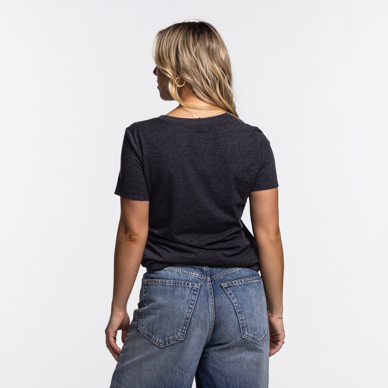 A person with blonde hair, wearing a Nike Miami HEAT Original Vice Nights Women's V-Neck Tee and blue jeans, faces away from the camera against a plain white background.