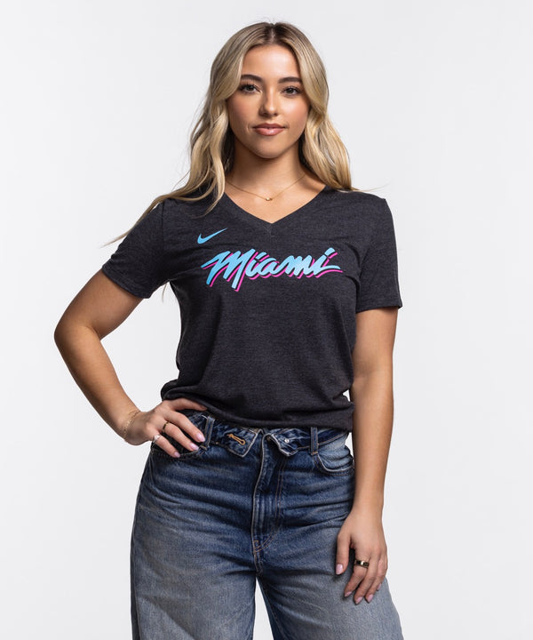 A woman with long blonde hair wears the Nike Miami HEAT Original Vice Nights Women's V-Neck Tee in dark gray with colorful 