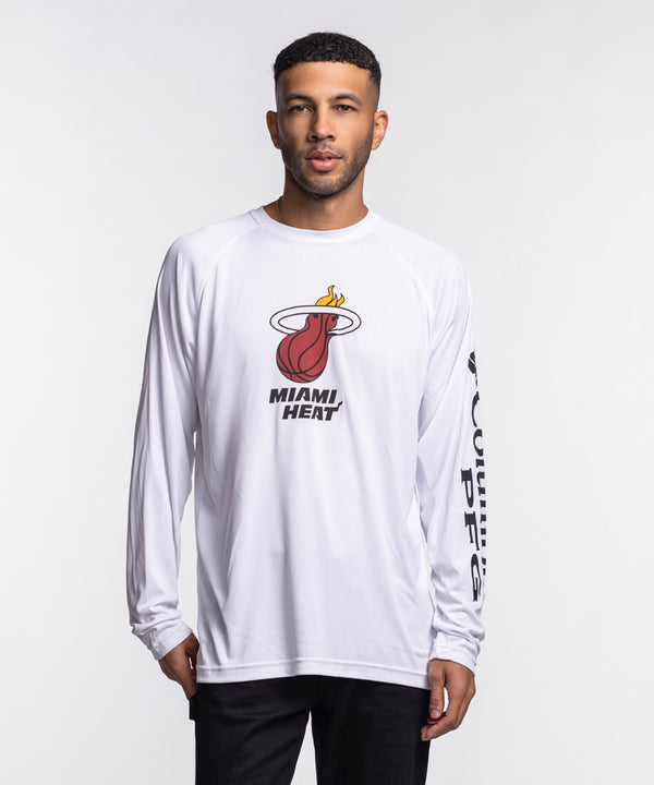 A man wearing a Columbia Miami HEAT Logo Terminal Long Sleeve Tee by Columbia Outdoor and black pants stands against a plain white background.