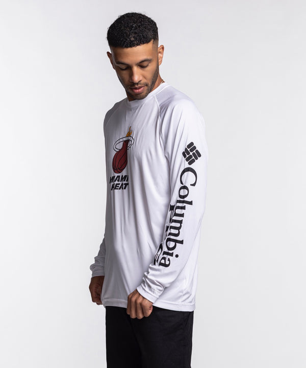 A man wearing a Columbia Miami HEAT Logo Terminal Long Sleeve Tee by Columbia Outdoor and black pants stands against a plain white background.