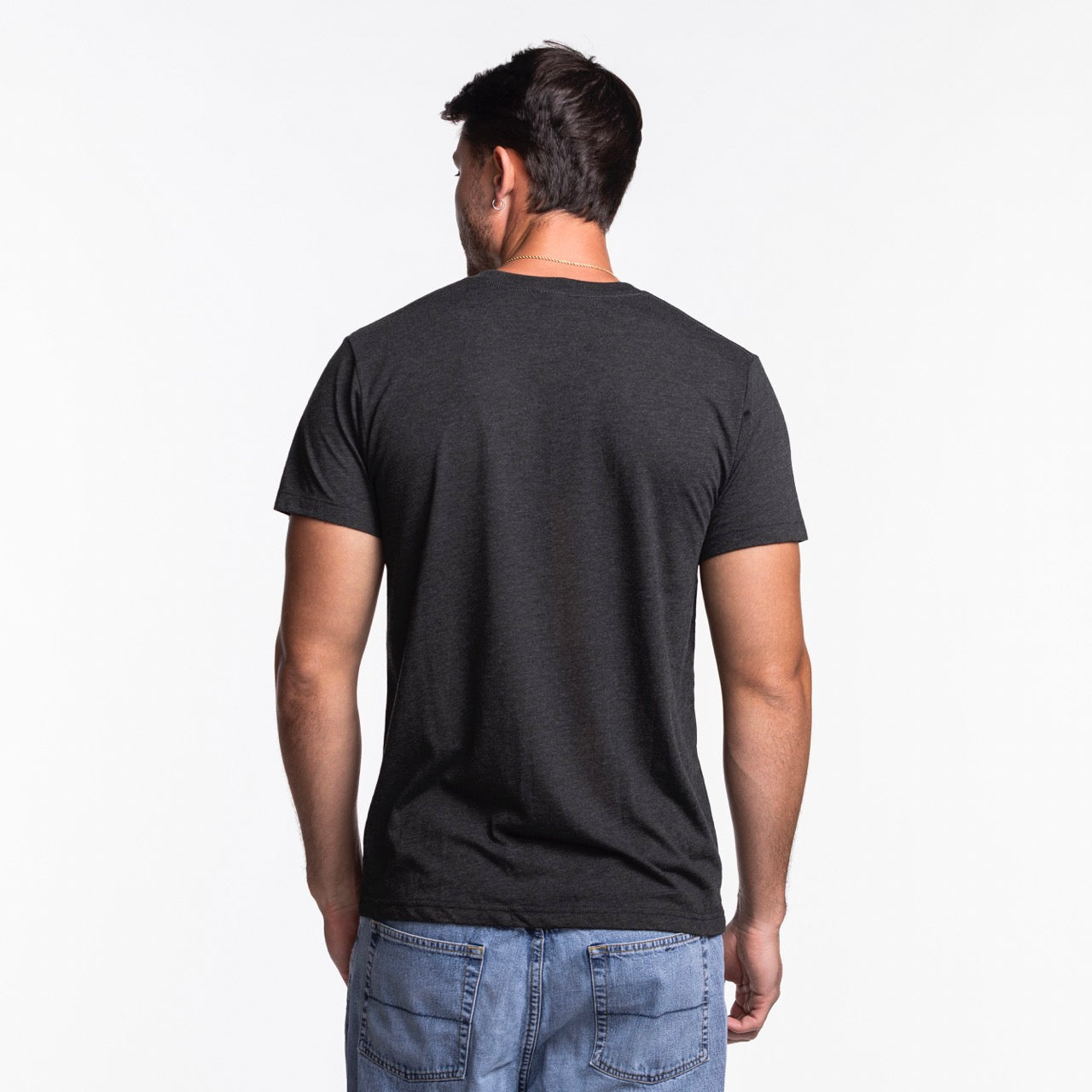 A man stands with his back to the camera, wearing the Homage Miami HEAT Snoopy Tee by Homage and blue jeans against a white background.