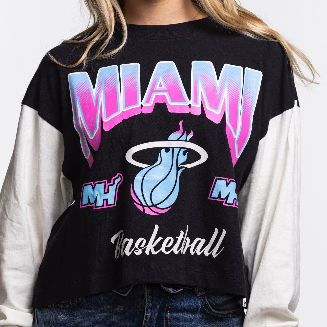 A person wears a '47 Brand Miami HEAT Original Vice Nights Women's Crewneck, featuring black and white cotton, MIAMI Basketball text, pink/blue/white flaming basketball logo, and Miami Heat graphics. Face not visible; machine washable.
